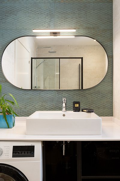 Modern bathroom with an oval mirror, sink, and built-in washing machine in a Barcelona apartment.